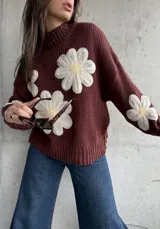 Sweater de punto color chocolate con diseño de flores grandes en relieve en color crema y centro amarillo. Presenta cuello alto, mangas largas y corte holgado.