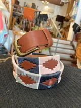 Cinturón de cuero en tono tostado con bordado a mano de hilos encerados en tonos marrones y beige con motivos geométricos, y hebilla metálica rectangular.