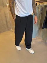 Pantalón sastrero de corte holgado, color negro, con pinzas frontales y cierre de cremallera.