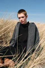 Chaqueta de punto con capucha, manga larga y cierre frontal con cremallera metálica. Presenta un diseño de tejido texturizado en color gris oscuro con detalles en contraste en los puños.