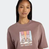 Remera cropped de manga corta, color marrón topo, con cuello redondo y un estampado frontal que muestra un par de zapatillas New Balance sobre un fondo de bloques de color degradados.