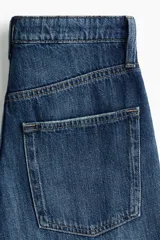 Jean de tiro alto con corte wide leg, confeccionado en denim de algodón rígido. Presenta diseño clásico de cinco bolsillos, cierre frontal con botón y acabado de lavado azul medio con efecto desgastado.