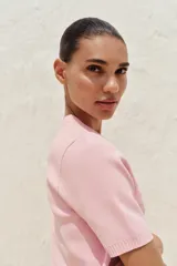 Chaqueta de punto color amarillo pálido, con cuello redondo, manga corta, cierre frontal con botones dorados y bolsillos de parche en el pecho.