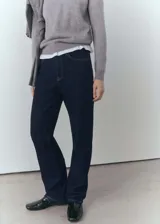 Jeans de corte recto y tiro medio, confeccionados en algodón con lavado oscuro (rinse wash). Presentan cierre de cremallera con botón, trabillas en la cintura, dos bolsillos laterales y dos bolsillos de parche en la parte posterior.