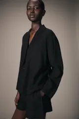 Camisa de estilo pijamero confeccionada en lino 100%, con cuello solapa de muescas, manga larga y cierre frontal con botones. Presenta un diseño de corte recto con bajo asimétrico.
