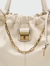 Bolso tipo tote de cuero color crema, con frunce superior y asas de hombro. Presenta un pequeño bolsillo frontal con cierre metálico dorado y un dije de llave colgante.