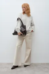 Sweater de punto en color beige melange, con cuello redondo y mangas largas. Presenta un diseño decorativo con perlas aplicadas en la parte frontal y en las mangas.