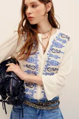 Camisa de color crudo con bordados en tonos azules de diseño paisley en el frente y las mangas. Presenta escote en V con abotonadura parcial y mangas largas.