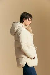 Campera acolchada de nylon en color crema, con capucha ajustable, cierre frontal con botones y cordón de ajuste en la cintura.