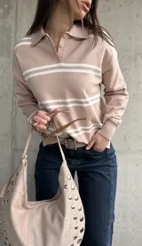 Sweater de punto con rayas horizontales blancas y base en tono beige y rosado, cuello polo con botones y mangas largas.