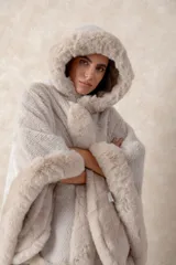 Capa de piel sintética en color negro, con diseño holgado, capucha integrada y bordes con textura de pelo largo.