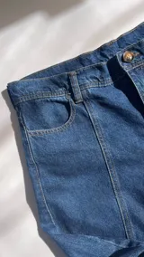 Jean de estilo recto y tiro medio-bajo confeccionado en denim azul marino oscuro. Presenta un diseño con costura vertical en la parte posterior de las piernas y bolsillos traseros clásicos. Esta prenda está elaborada con algodón reciclado bajo procesos de producción sostenible.