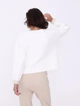 Sweater blanco de tejido de punto con cuello redondo y mangas largas. Tiene dos bolsillos cuadrados de lurex color beige en el frente.