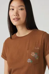 Remera color marrón con bolsillo en el pecho con bordado de flores y texto.
