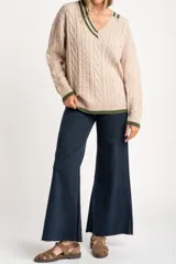 Sweater de lana y nylon color beige jaspeado, con diseño de punto trenzado (cable knit) en todo el cuerpo y mangas. Presenta cuello en V con ribete de dos franjas verdes y puños y bajo con ribete verde liso.