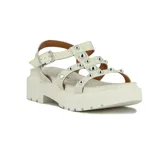 Sandalias de plataforma color blanco hueso, con tiras anchas adornadas con tachas metálicas redondas plateadas. Cuentan con cierre de hebilla ajustable en el tobillo y suela track gruesa.