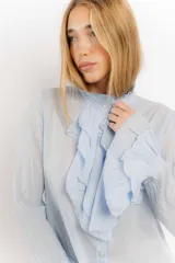 Camisa de algodón en color celeste, con cuello alto tipo victoriano, volados frontales y mangas largas con puños abullonados con volados.