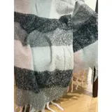 Bufanda rectangular de tejido grueso con diseño de cuadros en tonos azul, naranja, gris y beige, terminada con flecos en los extremos.