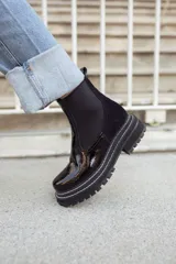 Botas tipo Chelsea con paneles elásticos laterales, confeccionadas en una combinación de cuero liso y gamuza en tonos marrones. Presentan una suela track robusta y dentada en color beige.
