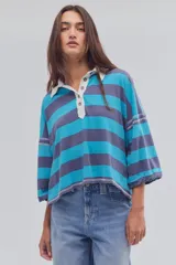 Remera tipo polo de algodón, de calce oversize, con diseño a rayas en tonos azul y celeste, cuello clásico blanco, botonadura corta, hombros caídos y mangas cortas.
