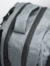 Mochila gris con cierre superior y bolsillo frontal con cierre. Tiene dos bolsillos laterales de red y logo de la marca en blanco en la parte superior.