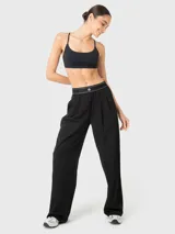 Pantalón de vestir negro de corte holgado y tiro medio, con cintura elástica estilo bóxer que presenta detalle de líneas blancas y logo bordado. Cuenta con pinzas delanteras y bolsillos laterales.
