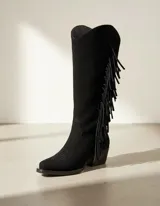 Bota de caña alta estilo western confeccionada en cuero vacuno color negro, con detalle de flecos laterales y taco cuadrado de madera.
