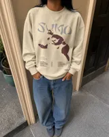 Buzo de cuello redondo color beige, con diseño gráfico en el frente que incluye la leyenda 'Sumo', una ilustración de un luchador de sumo y listado de canciones.