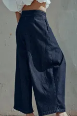 Pantalón tipo culotte de tiro alto confeccionado en denim azul oscuro. Presenta pinzas delanteras, pernera ancha y corta, bolsillos laterales ocultos y cierre frontal con cremallera, botón y ganchos.