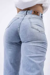 Jeans de mezclilla azul claro, tiro alto, corte wide leg y roturas a la altura de las rodillas.