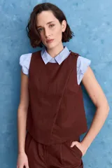 Top sin mangas color marrón, con cuello redondo y diseño cruzado en el frente. Presenta cierre con botones en el hombro y silueta recta de calce relajado.