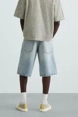 Bermuda de denim de algodón, color azul medio lavado, de corte ancho (baggy fit) y largo hasta la rodilla. Presenta cinco bolsillos y cierre frontal con cremallera y botón.