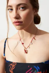 Collar con cordón trenzado rojo y blanco, adornado con dijes metálicos dorados de temática marina (pez, estrella de mar, caracola) y cuentas de coral rojo y perlas.