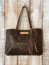 Cartera tipo tote de cuero con acabado desgastado en tonos marrones y negros. Presenta un cierre frontal metálico en color dorado y un detalle de borla de cuero colgante en el lateral. Posee doble asa de hombro.