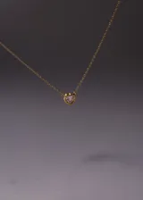 Collar de cadena tipo forcé con dije de corazón engastado con una piedra de cristal transparente. La pieza está fabricada en plata 925 con un baño de oro de 18k.