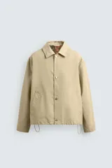 Cazadora de corte relajado confeccionada en denim de algodón color beige. Presenta cuello solapa, cierre frontal con botones metálicos, bolsillos de vivo en la cadera y bajo ajustable con elástico. El interior cuenta con un forro estampado a contraste.