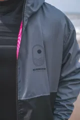 Campera con capucha de diseño impermeable, color gris en la parte superior y negro en la inferior, con cierre frontal y forro interior fucsia con estampa animal print. Presenta estampado gráfico de la marca Blue Moon en el pecho.