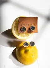 Aros tipo botón (studs) con piedras druzy negras o grises, engastadas en bisel dorado.