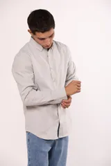 Camisa de manga larga en color gris, confeccionada en algodón, con cuello abotonado y cierre frontal de botones.