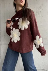 Sweater de punto color chocolate con diseño de flores grandes en relieve en color crema y centro amarillo. Presenta cuello alto, mangas largas y corte holgado.