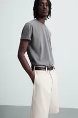 Bermuda color beige claro, de corte ancho y largo, confeccionada en algodón. Presenta cierre frontal con cremallera y botón, bolsillos laterales, bolsillo cerillero frontal y bolsillos traseros de vivo.