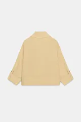 Chaqueta color beige con cuello solapa, manga larga remangada con trabilla y botón, y bolsillos de plastrón en el delantero. Cierre frontal con botones.