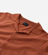 Camisa de punto jacquard color naranja, con cuello solapa, manga corta y cierre frontal con botones. Presenta detalles de rayas horizontales en contraste en el ruedo y en los puños de las mangas.