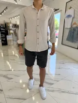Camisa de lino color tostado con sutiles rayas verticales blancas, cuello mao y mangas largas con puños vueltos. Cuenta con cierre frontal de botones oscuros.