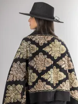 Pashmina de color negro con bordados ornamentales en hilos dorados y bronce. Presenta un diseño elegante con motivos florales y geométricos, ideal para usar sobre los hombros.