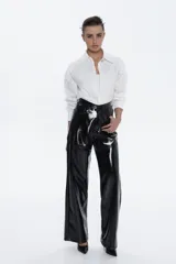 Pantalón de tiro alto, estilo wide leg, confeccionado en material sintético negro con acabado charol brillante. Presenta costuras verticales marcadas que definen la estructura.