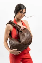 Bolso tipo hobo de cuero marrón con textura de piel de cocodrilo, asa anudada y cierre superior abierto.