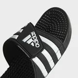 Ojotas Adidas Adissage negras con tres franjas blancas en la tira superior ajustable con velcro. La plantilla cuenta con protuberancias de masaje EVA.