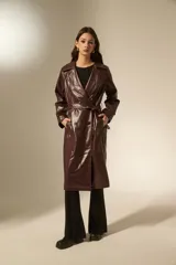 Trinchera de eco-cuero en color bordó, con diseño de doble botonadura, solapas amplias y cinturón ajustable en la cintura. Presenta mangas largas con detalles en los puños y bolsillos laterales.