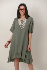 Vestido midi de lino color beige, con mangas cortas, cuello redondo, alforzas verticales en el pecho y detalle de volados en el ruedo.